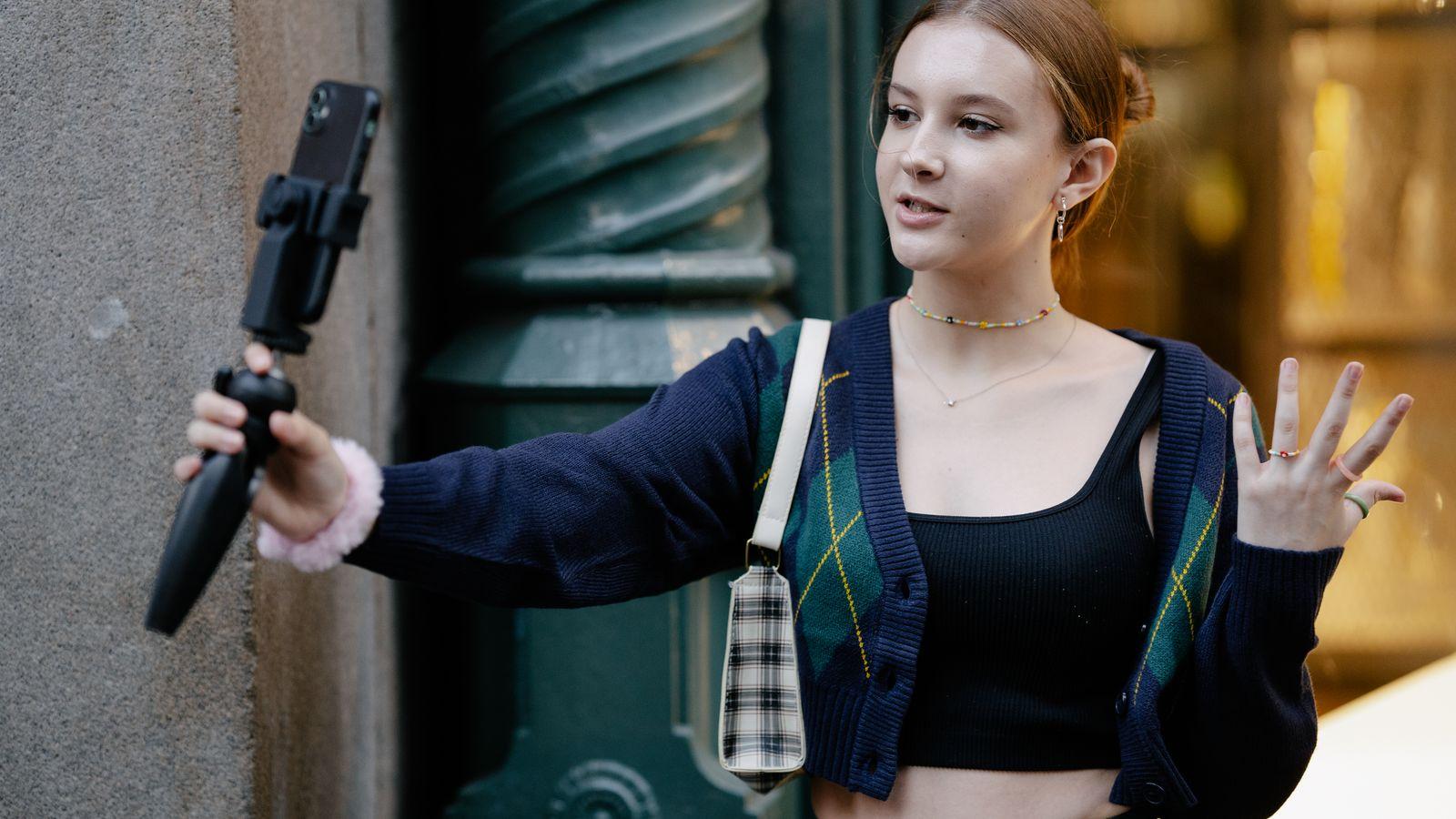 Filming herself with a phone on a mini tripod, city behind