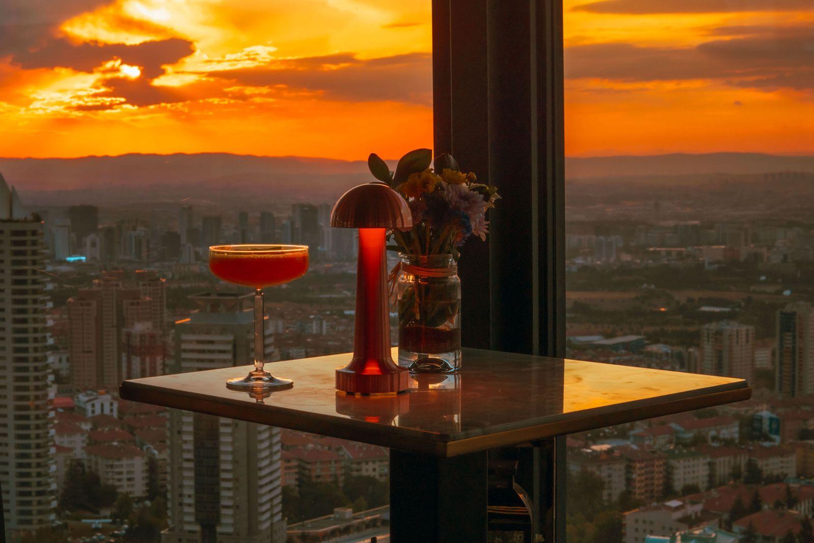A cocktail held up against a rooftop sunset