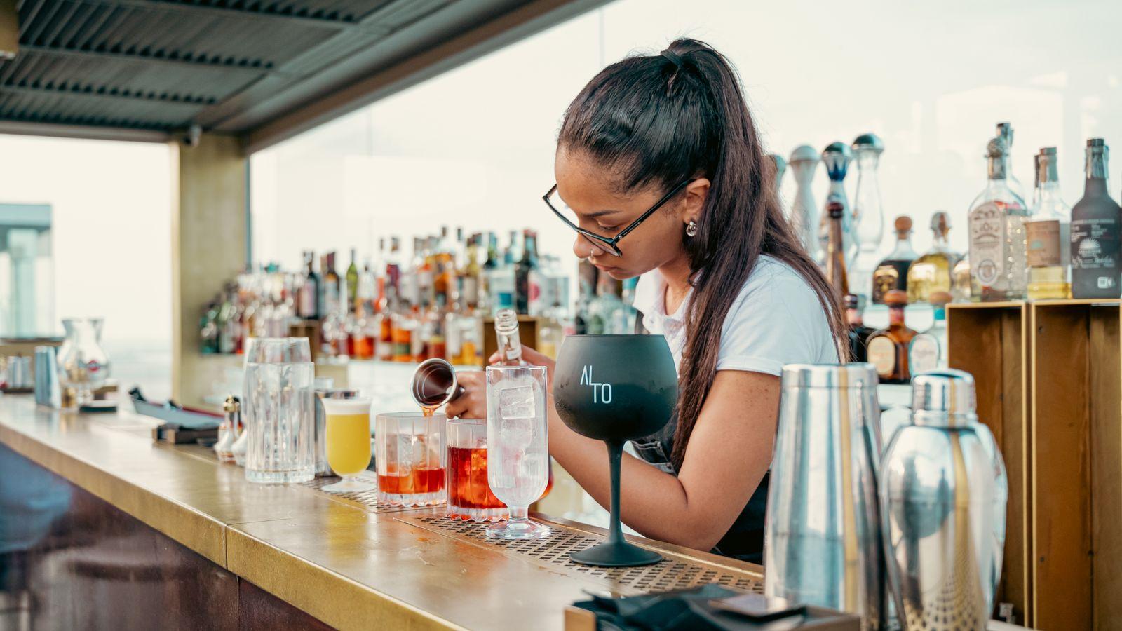Bartender mixing cocktails at a rooftop bar above the skyline