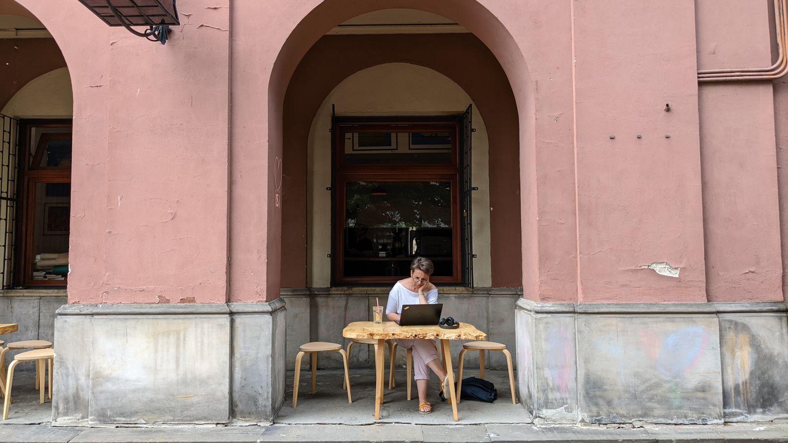 A creator working on her laptop at a sidewalk café table