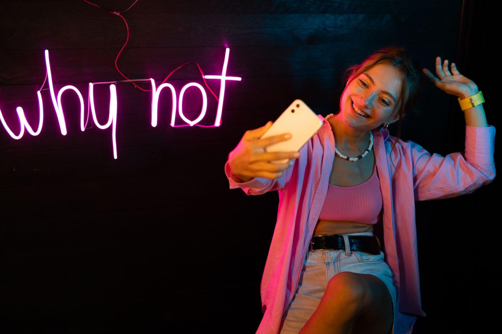 A creator framing a selfie under neon light