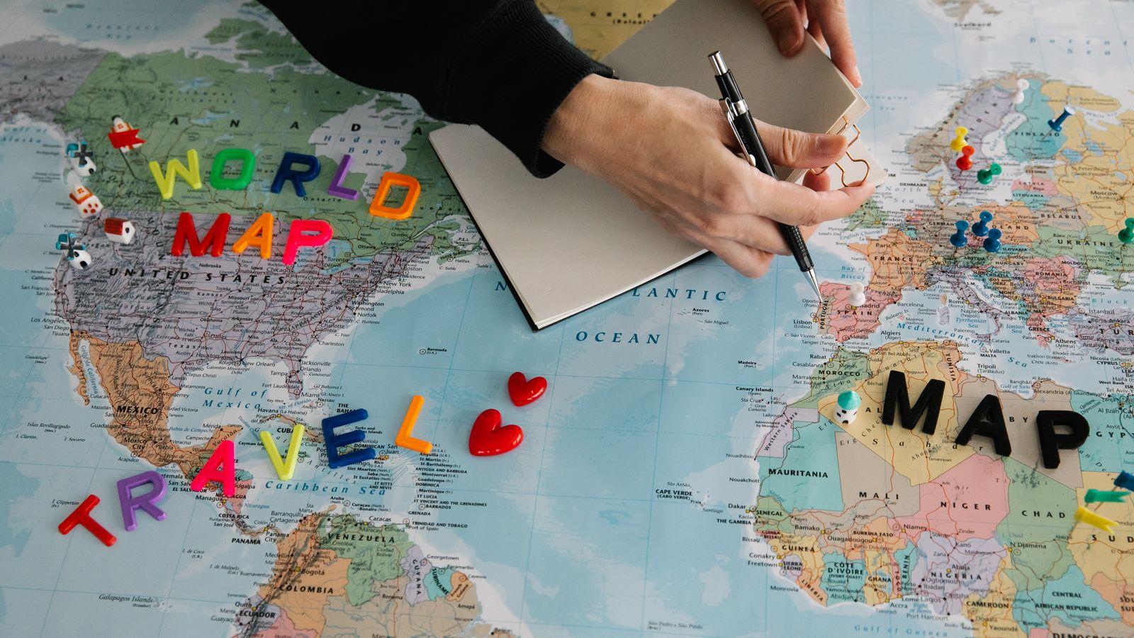 Hands plotting a journey on a world map, notebook ready